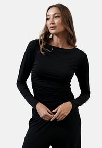 Czarny długi rękaw top wykonany z gładkiego materiału, z marszczeniem w talii. Prosty okrągły dekolt i dopasowane rękawy.