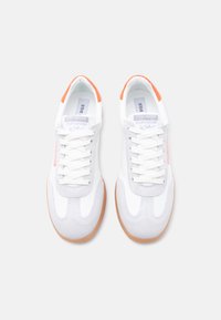 Paire de baskets Steve Madden blanches et grises avec semelles en gomme et détail talon orange, vues de dessus sur un fond blanc.