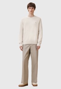 Helles beige Sweatshirt mit Rundhalsausschnitt und gerippten Bündchen, kombiniert mit hellbeigen, plissierten Hosen und lässigen Sneakers mit braunen Akzenten.