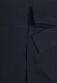 Tissu bleu marine à texture lisse, présentant une taille structurée et plissée avec un détail de couture au bord de la ceinture.