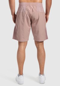 Herrars ljusrosa shorts i vävt tyg, med elastisk midja, sidofickor och en avslappnad passform. Bärs med vita sneakers.