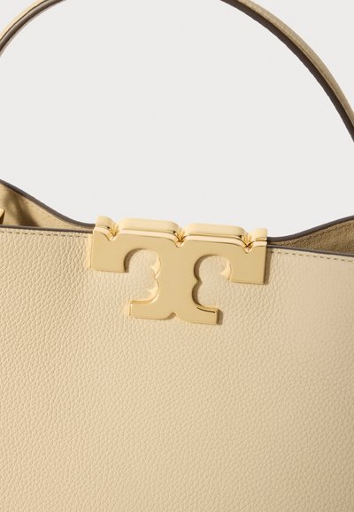 Beige leren handtas met een glanzende gouden logo-sluiting, een soepele textuur en een gestructureerde vorm met een contrasterende interieurkleur.