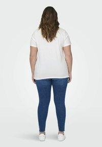 Biała koszulka krótki rękaw w połączeniu z niebieskimi obcisłymi dżinsami, noszona z białymi trampkami. Strój ma swobodny krój i prosty design.