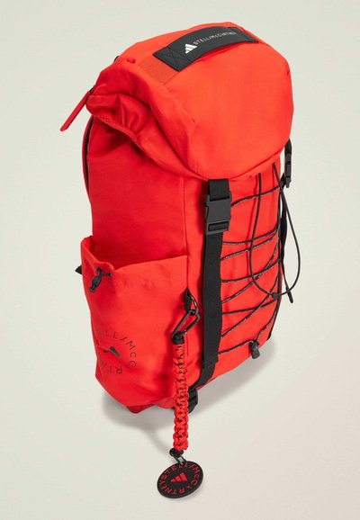 Red nylon backpack featuring a roll-top design, black accents, side pocket, elastic cord detail, and a logo patch on the top flap.