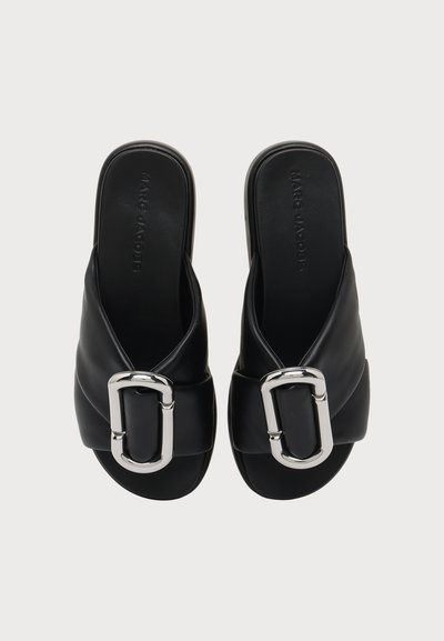 Paire de sandales noires à enfiler avec de grandes boucles argentées sur les brides avant, marque Marc Jacobs visible sur les semelles.