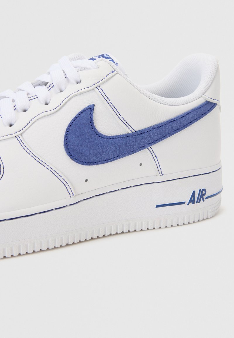 Baskets en cuir blanc avec des accents bleus. Présente un swoosh texturé bleu, des coutures contrastées et le logo "AIR" sur la semelle. Semelle en caoutchouc.
