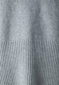 Grauer Strickpullover mit feinen und gerippten Texturen, der einen helleren grauen oberen Abschnitt und einen gerippten unteren Saum aufweist, was einen zweifarbigen Effekt erzeugt.