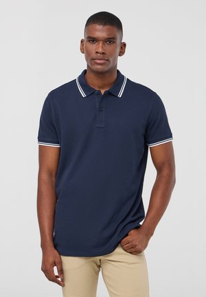 Polo shirt blu navy con colletto classico, con accenti a righe bianche sul colletto e sulle maniche, realizzato in un tessuto liscio e testurizzato.
