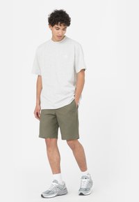 T-shirt in cotone grigio chiaro con scollo rotondo, abbinato a pantaloni corti verde oliva. Il modello indossa scarpe da ginnastica grigie e calze bianche.