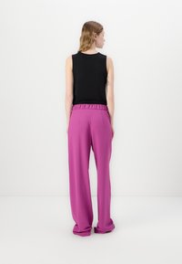 Zwarte mouwloze top gecombineerd met losse, hooggerokte broek in felroze. De broek heeft een gathered tailleband en een gladde textuur.