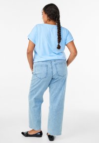 Modré bavlnené tričko s vyhrnutými rukávmi, v kombinácii s svetlomodrými širokými džínsami s pruhmi a čiernymi plochými topánkami. Džínsy majú zadné vrecká.