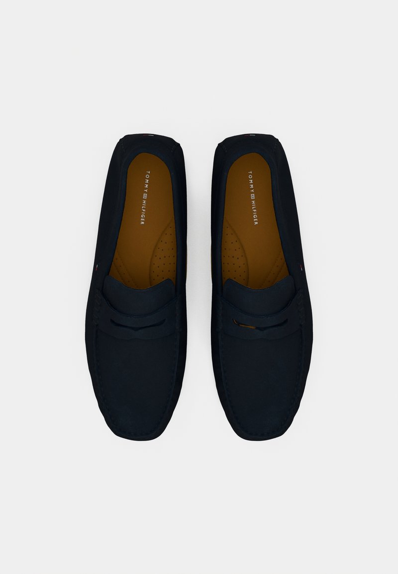 Ciemnoniebieskie loafersy wykonane z miękkiego materiału, z zaokrąglonym noskiem, kontrastującą brązową wkładką i dekoracyjnym przeszyciem.