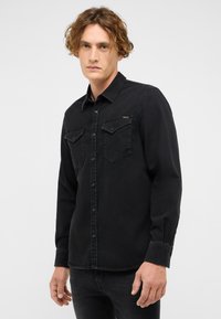 Czarna koszula dżinsowa z długimi rękawami, klasycznym kołnierzykiem, kieszeniami z przodu i guzikami. Charakteryzuje się miękką teksturą oraz prostym, czystym designem.