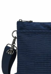 Mörkblå zip-väska med texturerad tyg, utrustad med en avtagbar rem och metallhardware. Har en framficka och glansiga accenter.