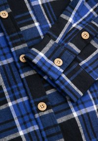 Koszula flanelowa w niebiesko-czarny wzór w kratę, z drewnianymi guzikami i miękkim, teksturowanym materiałem zapewniającym ciepło.