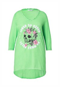 Robe t-shirt verte avec un col en V, manches 3/4, bord frangé, présentant un graphique de crâne noir entouré de roses roses et de texte.