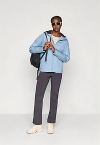 Šviesiai mėlyna striukė su užtrauktuku ir gobtuvu, derinama su tamsiai pilkomis kelnėmis. Modelis dėvi baltus batus ir akinius nuo saulės, rankoje laiko juodą kuprinę.