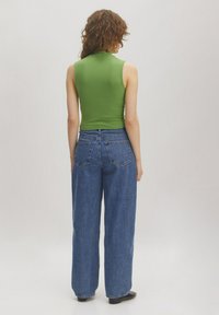 Groen geribbeld mouwloos topje gecombineerd met losse blauwe denim jeans. De stof is glad met een zachte textuur. Eenvoudig ontwerp en stiksels aan de achterkant.