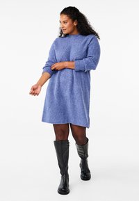 Vestido de punto en azul claro con un cuello alto, mangas largas y un patrón de diamante texturizado; combinado con botas negras hasta la rodilla.