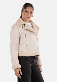 Giacca in ecopelle beige con colletto in shearling, chiusura con zip, tasche laterali e cintura regolabile. Design cropped con texture morbida.