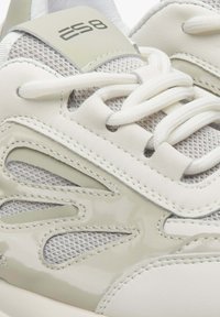 Sportschoenen met een lichtbeige leren en mesh bovenwerk, voorzien van een glanzende accent, een gestructureerd ontwerp en platte witte veters.