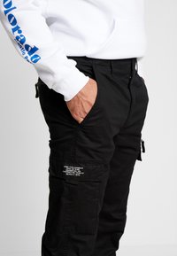 Zwarte cargobroek met meerdere zakken, gemaakt van duurzaam materiaal. Bevat een label op de been, ontworpen voor functionaliteit en comfort.