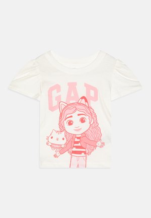 Λευκό βαμβακερό T-shirt με ροζ γραφικό σχέδιο που απεικονίζει έναν χαρακτήρα που κρατά μια γάτα και τη λέξη "GAP" σε έντονες ροζ γραμμές. Κοντά μανίκια.