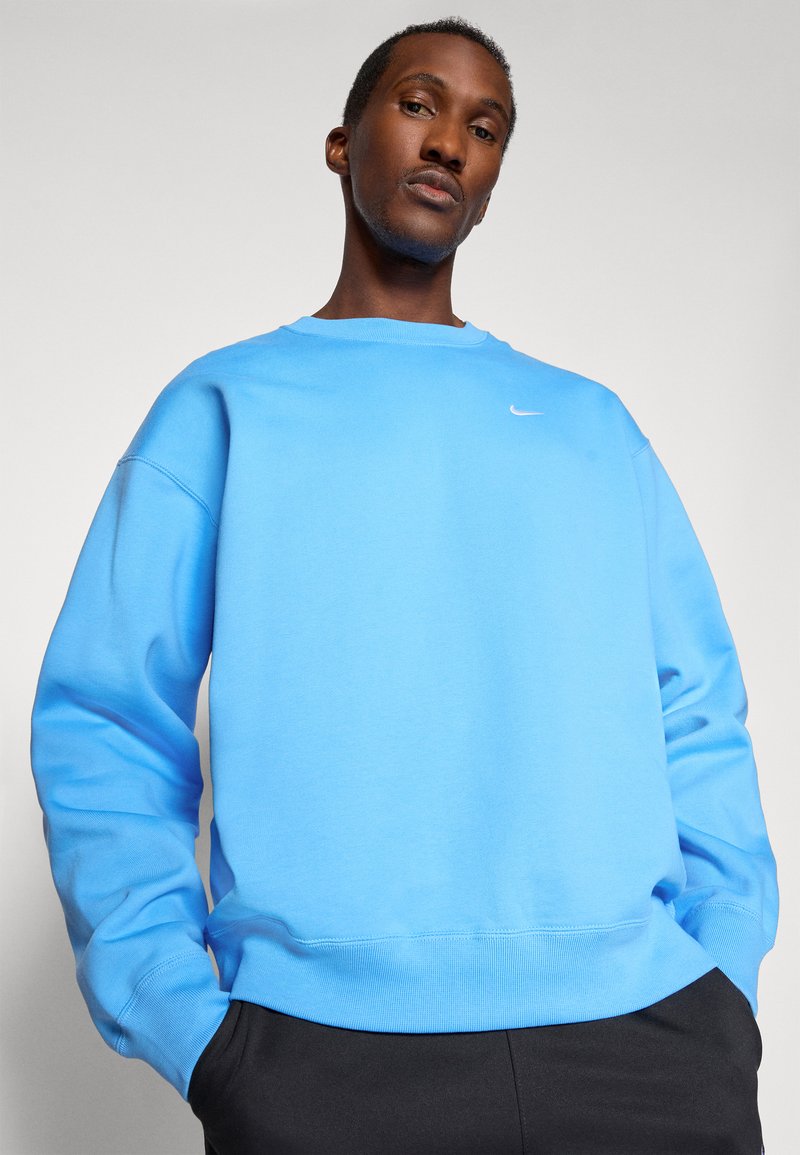 Jasnoniebieska bluza z bawełnianego materiału, z okrągłym dekoltem i ściągaczami na rękawach, z małym białym logo Nike na lewej piersi.