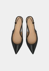 Chaussures plates à bouts pointus avec bride arrière noires, ornées de clous dorés sur les bords et semelles intérieures beiges, sur fond blanc.