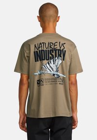 Olive green t-shirt featuring "NATURE VS INDUSTRY" text and a butterfly graphic on the back, with a soft, cotton texture.