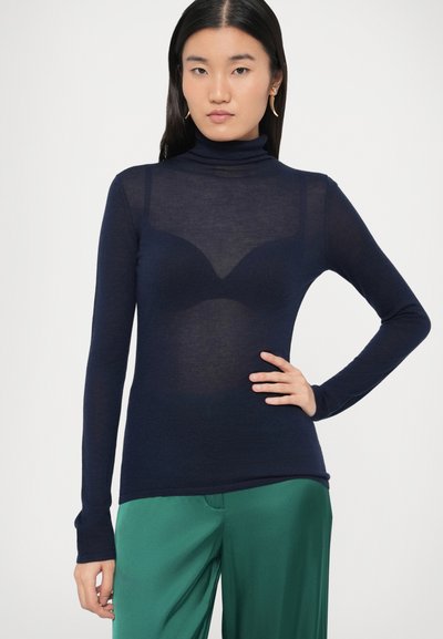 Meresinine kaelusega turtleneck-top läbipaistvast kangast ja pika varrukaga, kandmiseks tumedama aluskihi kohal, roheliste pükstega. Sile tekstuur.