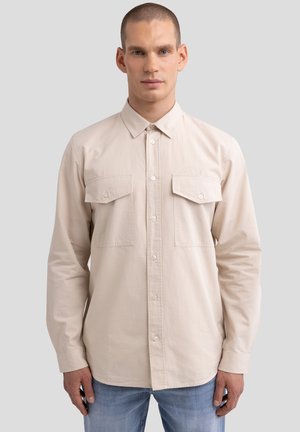 Light beige long-sleeve shirt with button-down collar, two chest pockets, and button closure, made from soft cotton fabric.