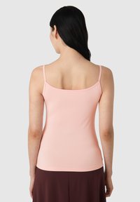 Jasnoróżowa, dopasowana koszulka bez rękawów z cienkimi ramiączkami i kwadratowym tyłem, wykonana z gładkiego, elastycznego materiału. Wykończona bezszwowym dołem.