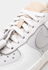 White and light gray sneaker with textured leather and suede accents, white laces, and a beige heel tab featuring embossed logo.