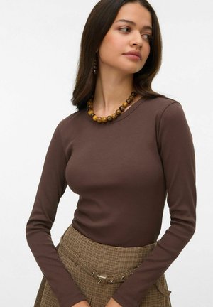 Bruine, geribbelde top met lange mouwen en ronde halslijn, gecombineerd met een geruite rok en een ronde kralenketting gemaakt van verschillende materialen.