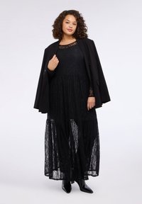 Czarna sukienka maxi z koronką, o warstwowym kroju i długich rękawach, zestawiona z czarną marynarką i botkami na szpic.