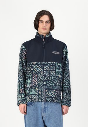 Fleece-pullover med høy krage; marineblå øverste del, mønstret nedre del i turkis, rosa og marineblå. Har en glidelås foran og logo-detalj.