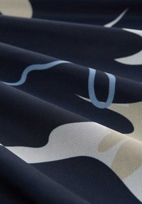 Kankaita tumma sininen, jossa on sileät, abstraktit vaaleanbeige ja siniset kuviot. Materiaali näyttää hieman läpikuultavalta ja siinä on kudottu pinta.