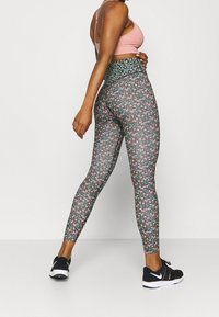 Leggings florales de cintura alta con un fondo oscuro que presenta pequeñas flores rosas y azules, combinados con un sujetador deportivo rosa claro y zapatillas negras.