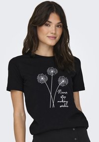 Svart bomulls t-skjorte med hvit dandelion-grafikk og teksten "Aldri slutt å lage ønsker." Korte ermer, rund hals.
