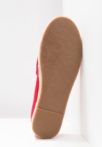 Semelle d'une chaussure plate rouge avec une semelle en caoutchouc brun clair montrant le nom de la marque en relief et la taille 37.