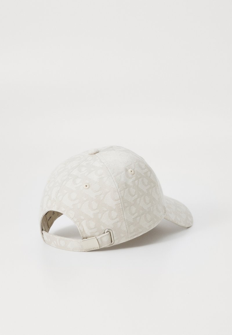 Gorra de béisbol beige con un sutil patrón en toda la superficie, correa ajustable en la parte posterior y un acabado de tela suave y texturizada.