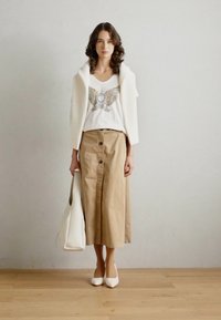 Beige knappet midi-skjørt, hvit tank topp med grafikk, ribbet hvit cardigan, hvit veske og spisse hæler. Glatt tekstur, uformell design.