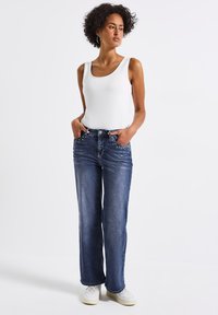 Jean denim bleu foncé avec une coupe droite, ornés d'accent en clous sur les poches avant. Associés à un débardeur blanc et des baskets.