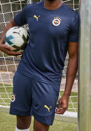 Tmavě modrý dres Puma na fotbal s texturovaným vzorem, žlutým logem a emblémem Fenerbahçe; odpovídající šortky se stejným vzorem a logem.