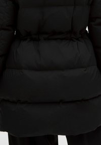 Giubbotto nero imbottito con sezioni trapuntate, una texture liscia e un taglio a lunghezza media, progettato per il calore e l'isolamento.