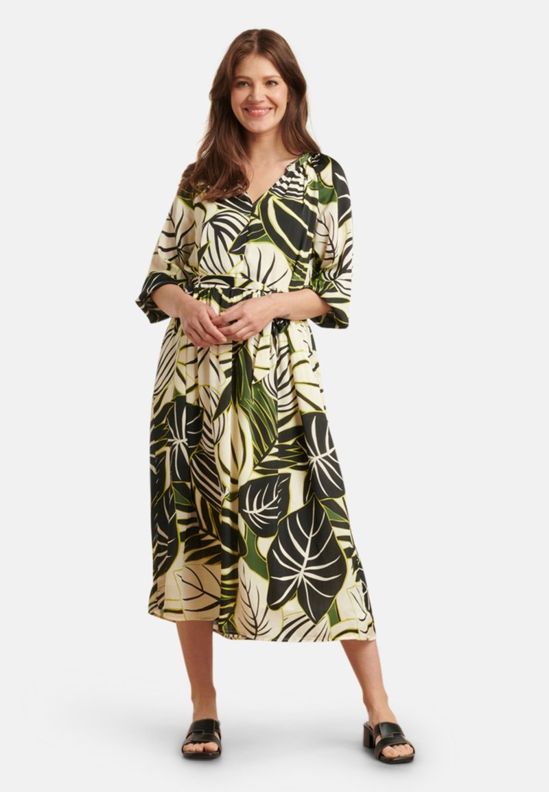 Blumenkleid in Weiß mit schwarzen und grünen Blättermustern, Drei-Viertel-Ärmeln und einem Bindegürtel. Glattes Material und mittellang geschnitten.