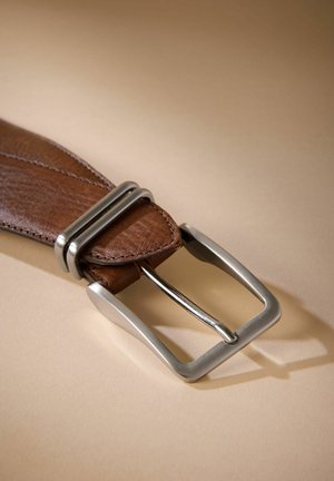 Hnedý kožený opasok s textúrovaným povrchom, s obdĺžnikovou striebornou sponou a dvoma kovovými hrotmi, na béžovom pozadí.