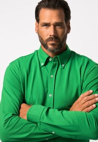 Groene langetekraagshirt met knoopsluiting, gemaakt van zachte stof. Voorzien van witte knopen en een relaxte pasvorm.