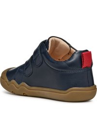 Marinblå lädersko med två kardborreband, tanfärgad gummisula och röd tygflik på hälen. Rund tå och slät yta.